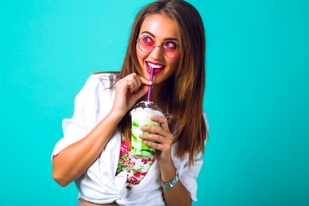 Belle jeune femme en mini short en jean, boire un smoothie savoureux, tenue vintage, maquillage lunettes de soleil