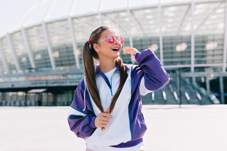 Belle jeune femme à la mode dans des vêtements élégants portant des lunettes de soleil roses et riant