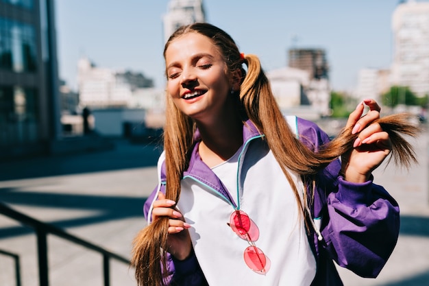 Belle jeune femme à la mode posant avec un beau sourire et les yeux fermés au soleil du matin