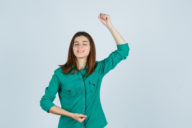 Belle jeune femme montrant le geste du gagnant en chemise verte et à la béatitude. vue de face.