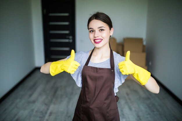 Belle jeune femme montrant le pouce vers le haut et tenant des produits de nettoyage pour fenêtre