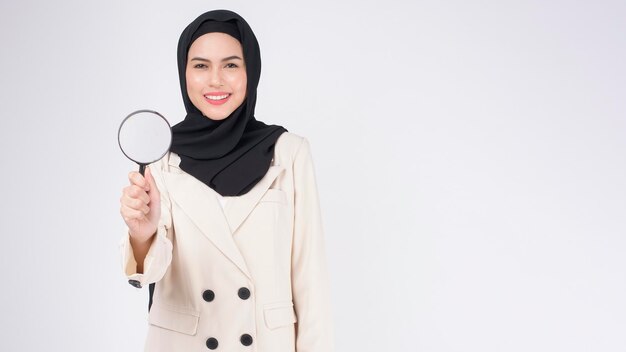 Belle jeune femme musulmane en costume tenant une loupe sur fond blanc studio