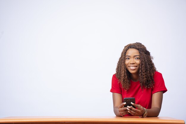 Belle jeune femme noire assise à un bureau et à l'aide de son téléphone