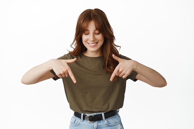 Photo gratuit belle jeune femme pointant du doigt et regardant vers le bas avec un visage heureux, a trouvé une publicité intéressante ci-dessous debout sur blanc