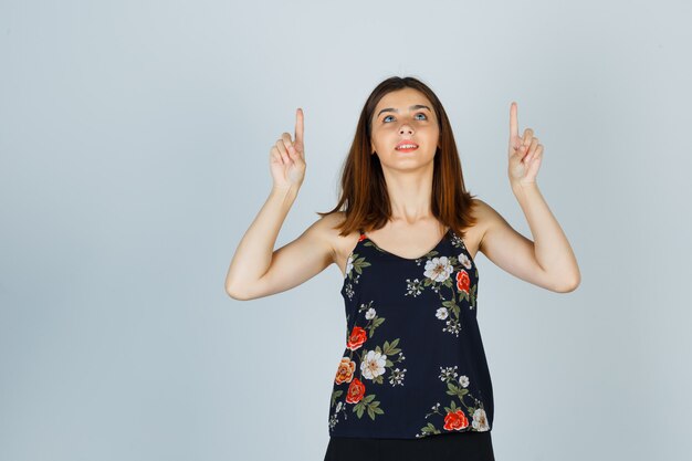 Belle jeune femme pointant vers le haut en chemisier, jupe et à la joyeuse