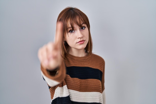 Photo gratuite belle jeune femme portant un chandail rayé sur fond isolé pointant du doigt vers le haut et une expression de colère ne montrant aucun geste