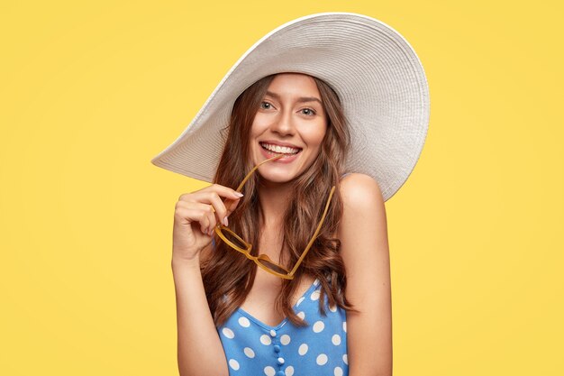 Belle jeune femme portant un chapeau posant contre le mur jaune