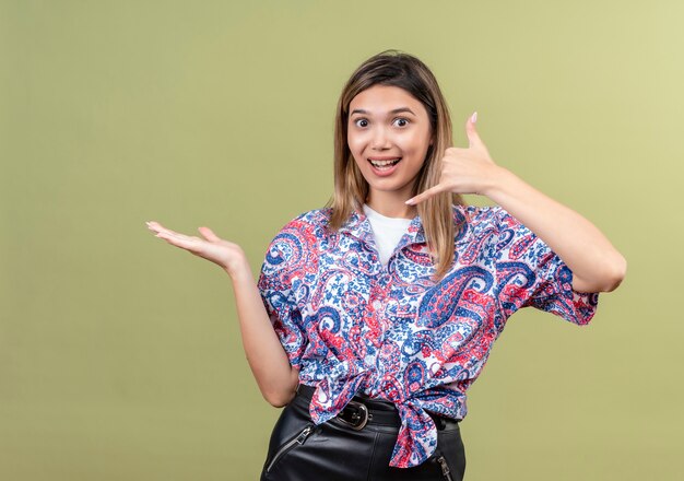 Une belle jeune femme portant une chemise imprimée paisley montrant appelez-moi geste