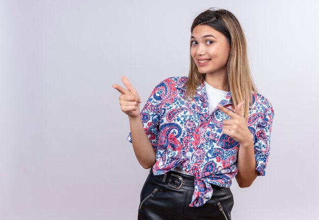 Une belle jeune femme portant une chemise imprimée paisley pointant avec l'index tout en regardant sur un mur blanc