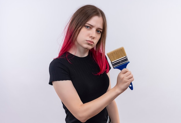 Belle jeune femme portant un t-shirt noir tenant un pinceau sur un mur blanc isolé