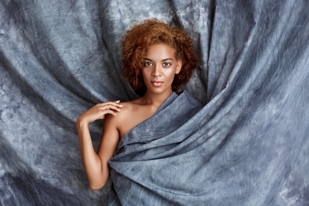 Belle jeune femme posant, enveloppé dans un tissu gris