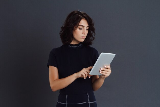 Belle jeune femme posant sur un mur gris et tenant la tablette dans les mains