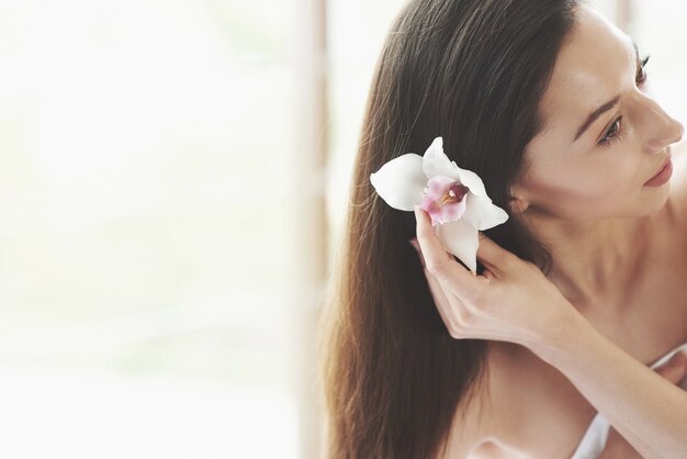 Belle jeune femme posant avec orchidée. Traitement de soins de la peau.