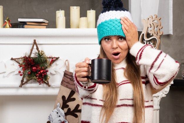 Belle jeune femme posant avec une tasse de thé près de la cheminée.