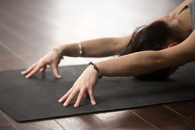 Belle jeune femme en pose de Balasana, fond de plancher de studio