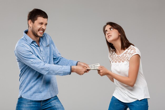 Belle jeune femme prenant de l'argent de l'homme sur le mur gris