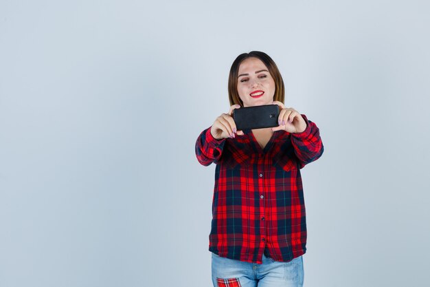 Belle jeune femme prenant selfie en chemise décontractée et semblant joyeuse. vue de face.