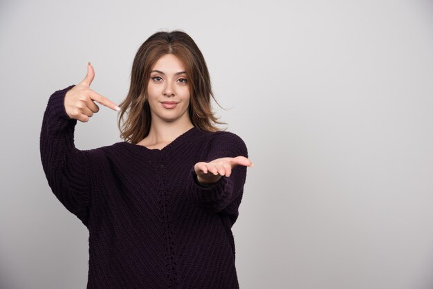 Belle jeune femme en pull tricoté chaud pointant vers sa main.