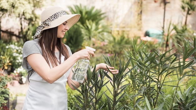 Photo gratuite belle jeune femme pulvérisant de l'eau de bouteille sur les plantes en croissance