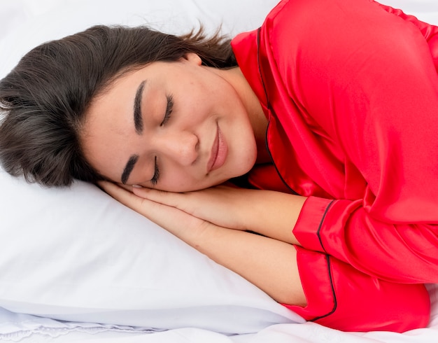 Photo gratuite belle jeune femme en pyjama rouge se détendre dans son lit