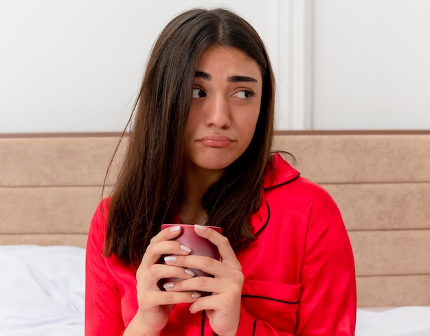 Belle jeune femme en pyjama rouge se détendre dans son lit