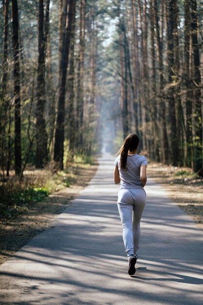 Belle jeune femme qui court dans un parc verdoyant sur une journée d'été ensoleillée