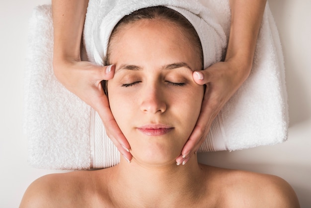 Photo gratuite belle jeune femme recevant un massage du visage avec les yeux fermés dans un salon spa