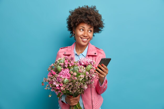 Belle jeune femme réfléchie reçoit des félicitations sur le smartphone fête son anniversaire obtient un joli bouquet de fleurs