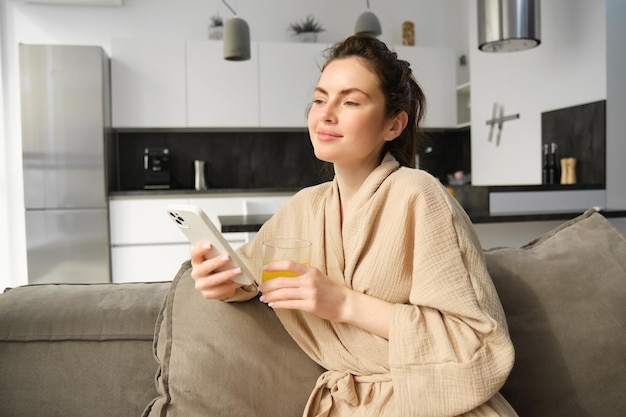 Photo gratuite belle jeune femme reposant sur un canapé profitant de sa matinée à la maison tenant un verre de jus d'orange et