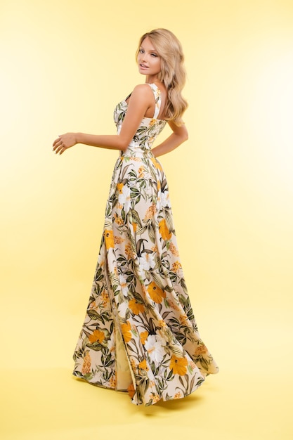 Photo gratuite belle jeune femme en robe lon pose pour la caméra, photo isolée sur fond jaune
