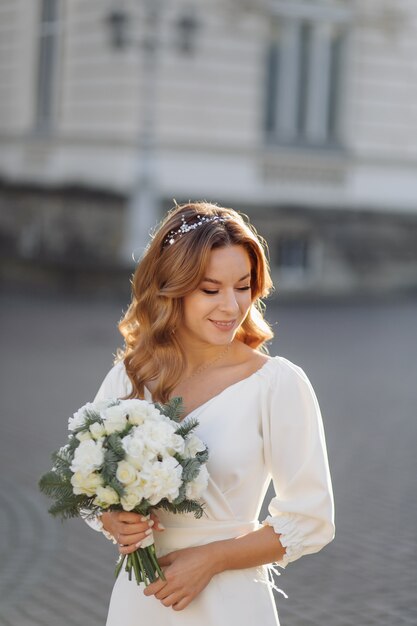 Belle jeune femme en robe de mariée posant dans la rue en ville