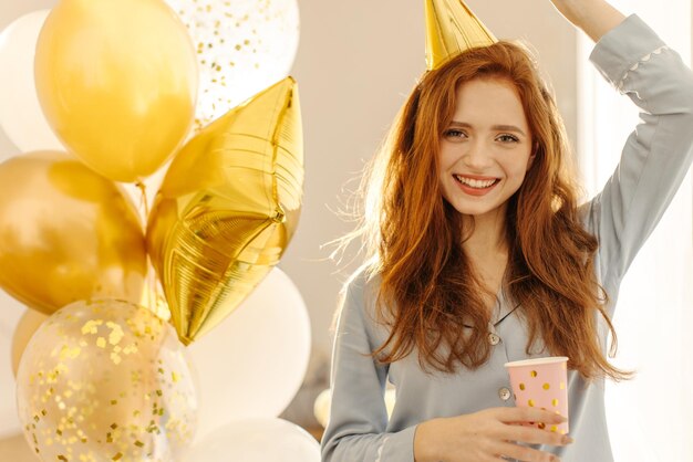 Belle jeune femme rousse caucasienne en vêtements de maison fête son anniversaire avec des ballons Concepts de fête