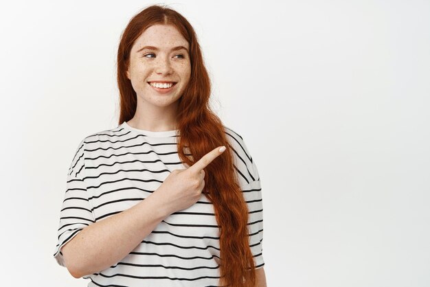 Belle jeune femme rousse fille avec des taches de rousseur regardant et pointant le doigt à la vente montrant le signe de lecture de publicité de coin supérieur droit avec un sourire heureux fond blanc