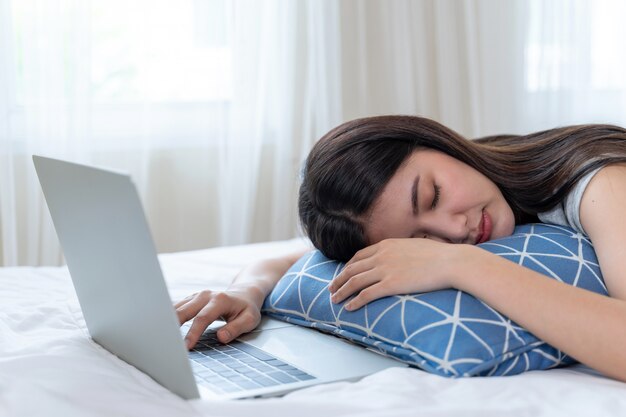 Belle jeune femme s'est endormie sur le lit après la fatigue de travailler avec un ordinateur portable