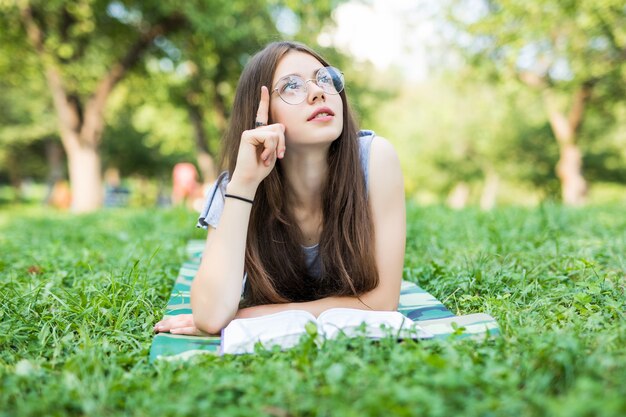 Belle jeune femme s'étend sur un champ vert et lit le livre.