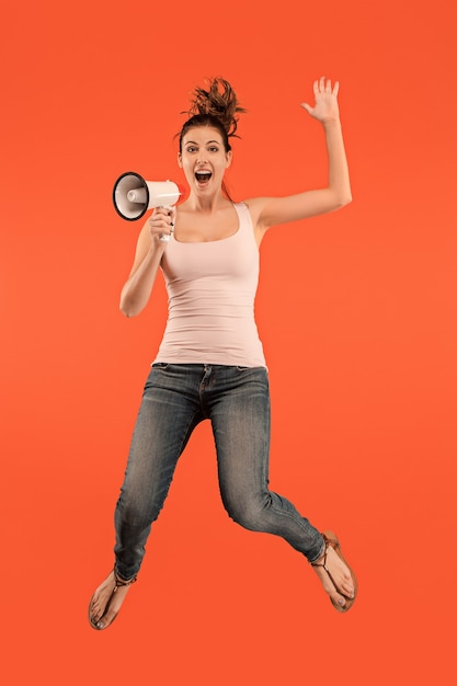 Belle jeune femme sautant avec mégaphone isolé sur fond rouge. Fille runnin en mouvement ou en mouvement