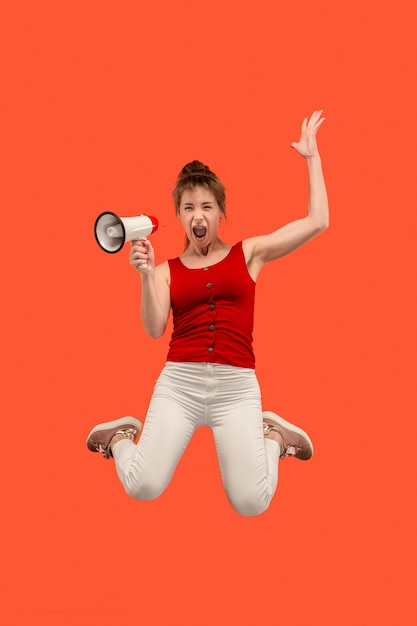 Belle jeune femme sautant avec mégaphone isolé sur fond rouge