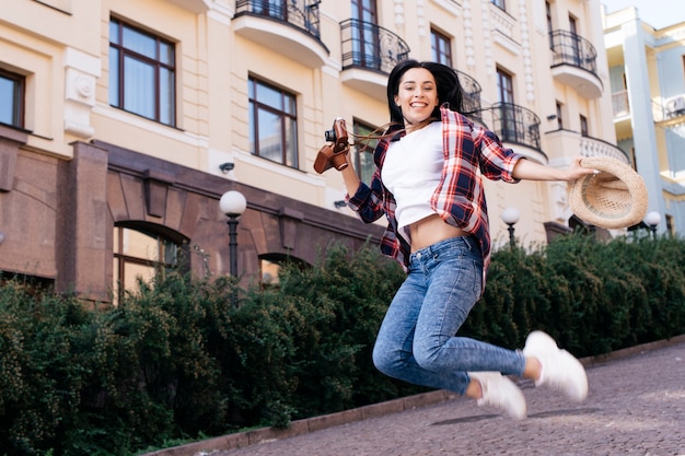 Photo gratuite belle jeune femme sauter dans la rue avec chapeau et caméra