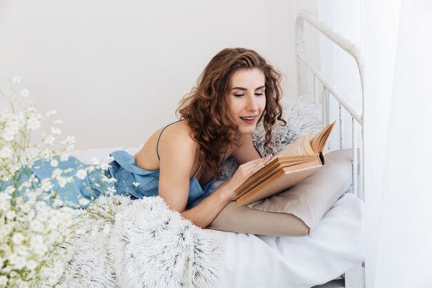 Belle jeune femme se trouve à l'intérieur dans le lit, lecture de livre