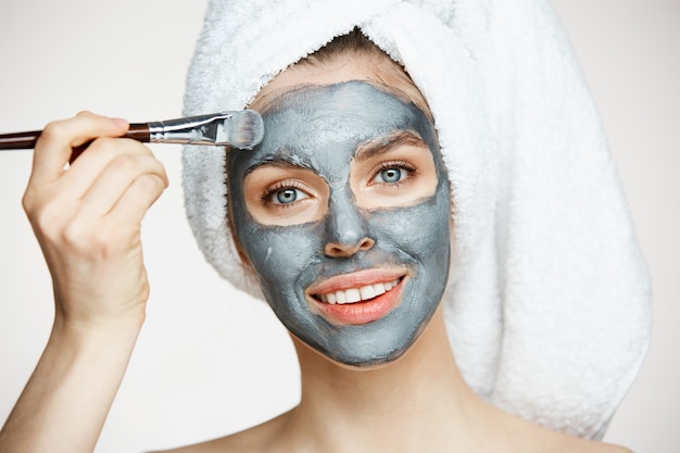 Belle jeune femme en serviette sur la tête couvrant le visage avec un masque souriant. Cosmétologie de beauté et spa.