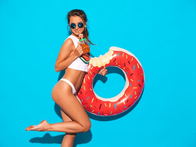 Belle jeune femme sexy souriante à lunettes de soleil. Fille en slip d'été blanc et sujet avec matelas gonflable donut lilo. . Boire une boisson fraîche de cocktail