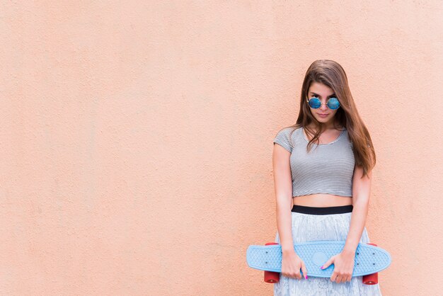 Belle jeune femme avec skateboard sur fond rose