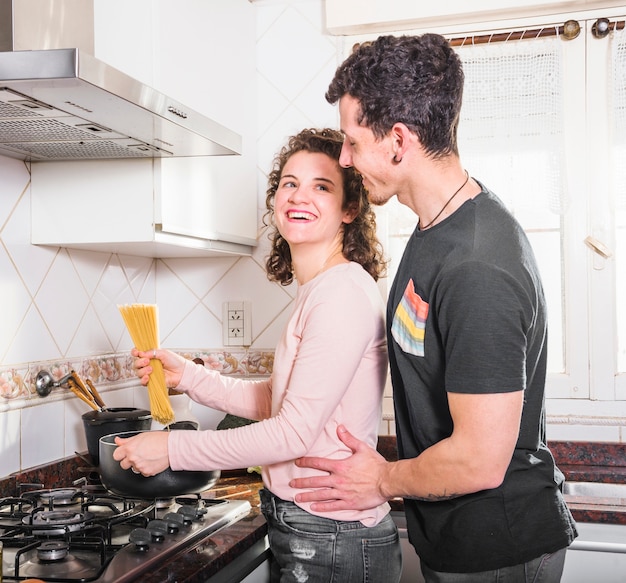 Belle jeune femme souriante prépare des spaghettis en regardant son mari