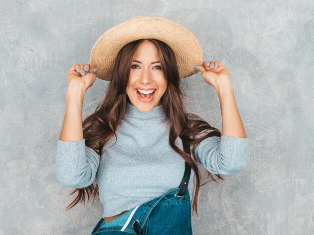 Belle jeune femme souriante à la recherche. Fille à la mode dans des vêtements de salopette d'été décontractée et un chapeau.