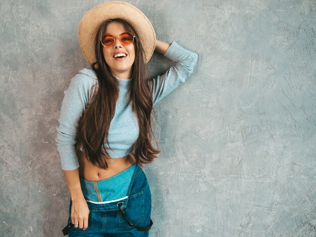 Belle jeune femme souriante à la recherche. Fille à la mode dans des vêtements de salopette d'été décontractée et un chapeau.