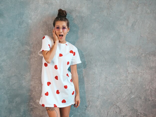 Belle jeune femme surprise regardant avec les mains près de la bouche. Fille branchée en robe blanche d'été décontractée.