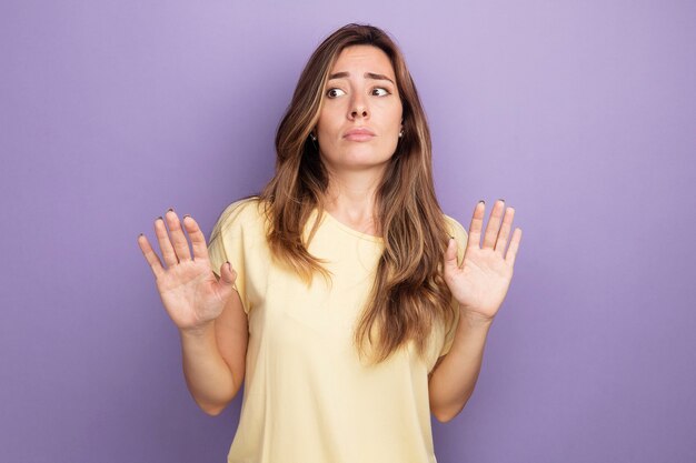 Belle jeune femme en t-shirt beige à côté confus tenant les mains comme dire ne vous approchez pas