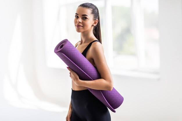Belle jeune femme avec un tapis de yoga au gymnase