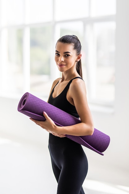 Belle jeune femme avec un tapis de yoga au gymnase