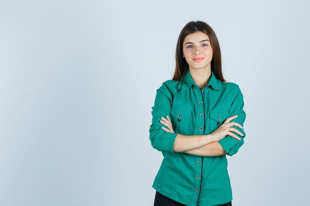 Belle jeune femme tenant les bras croisés en chemise verte et à la recherche positive. vue de face.